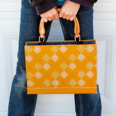 A woman holding a large purse at waist level.