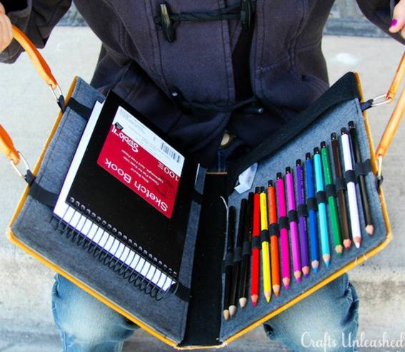 A person is holding and opening the art case box with colorful pencils and note pad.