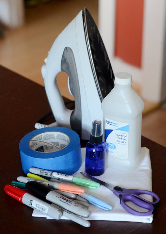 An iron sits beside some markers, a bottle of rubbing alcohol, scissors and masking tape.