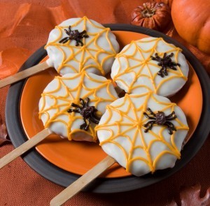 Spiderweb cookies with spiders and popsicle sticks on a plate.
