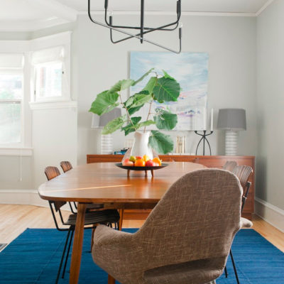 A dining table sits on a blue rug with a sideboard behind it.