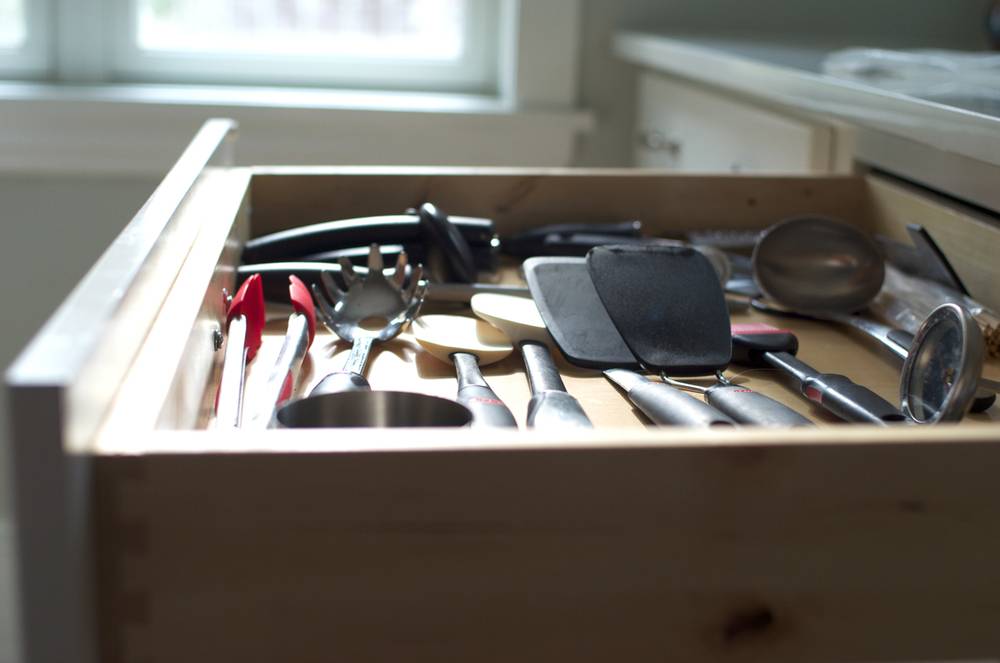 A kitchen drawer is open and exposes all of the tongs, spatulas, spoons and measuring cups inside.
