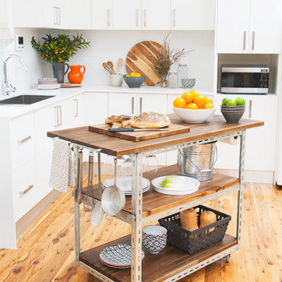 A kitchen trolley with food on it is in a kitchen with white counters and cabinets.