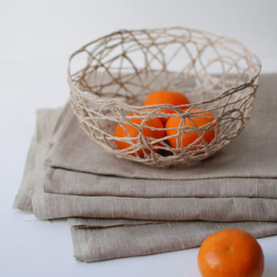 Oranges sit in a wicker basket on a grey material.