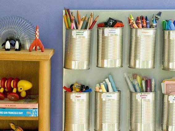 Tin cups glued to a poster board with writing utensils grouped inside next to a shelf of toys.
