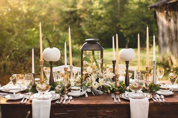 Dining table decorated with flowers, pumpkins, candles, plates, spoons, forks, glasses and cups.