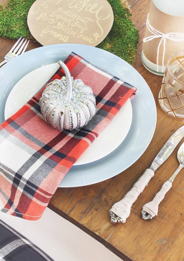 Pumpkin on top of a plaid napkin with a plate and silverware.