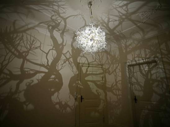 A chandelier is hanging from the roof in a forest like room.