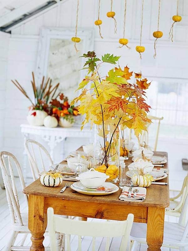 A wooden table decorated with dining set and a vase having fresh leaves.