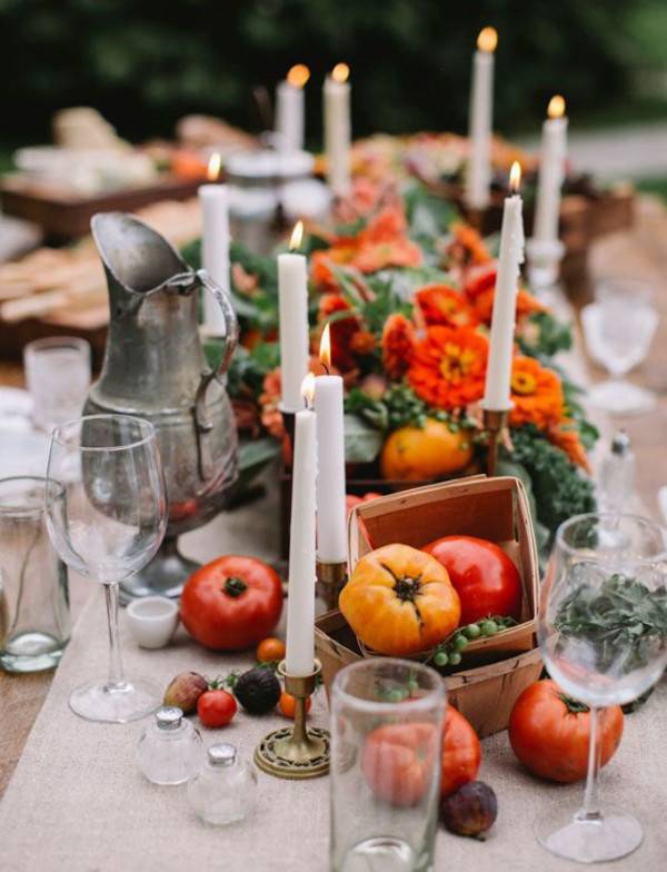 Tomatoes in a basket with candles and fall decorations on a table.