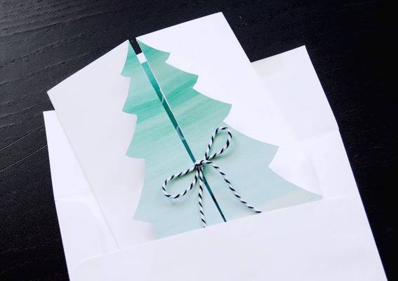 A Christmas tree in the center of a card that is folded in half and closed in the center with with ribbon