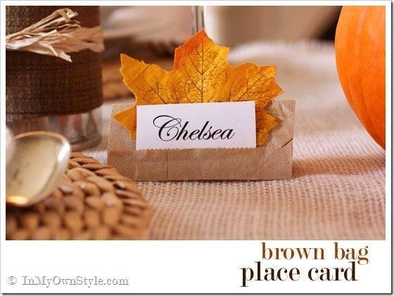 A place card is backed by a maple leaf and held by a folded brown piece of paper.
