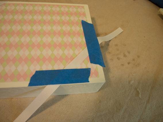 A piece of white painted wood has a plaid pastel design and is being further decorated.