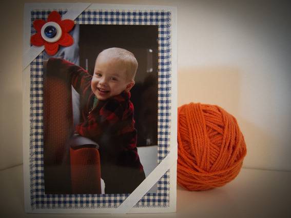 A photograph of a baby next to a ball of orange yarn.