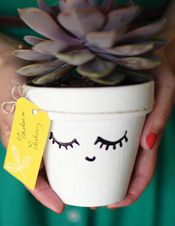 A person is holding a plant in a white container with a face on it.