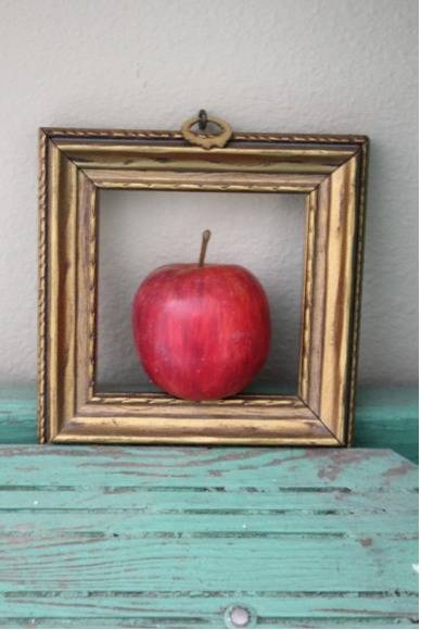 A red apple sitting in a gold frame against a wall.