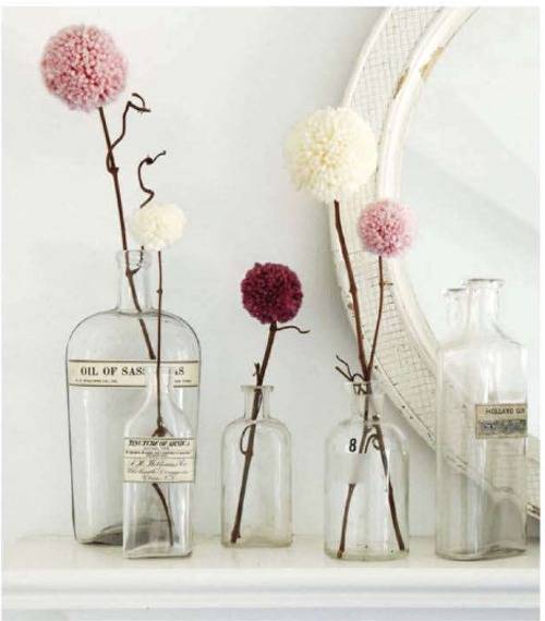 Single flowers in glass jars near an oval mirror on a shelf.
