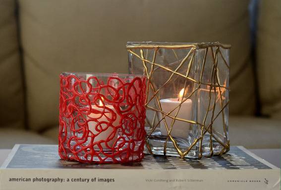 Two different votive candle holders made of hot glue, one red and cylindrical and the other square with gold piping.