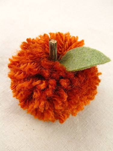 A fabric apple has been constructed with yarn, a piece of a twig and a paper leaf.