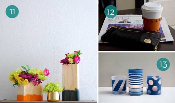 A light box with an orange bottom has flowers in it next to a gold cup with greenery in it next to a tall wooden box with a green bottom has flowers in it, a cup of coffee, a black hand bag, a newspaper, three blue and white lit candles.