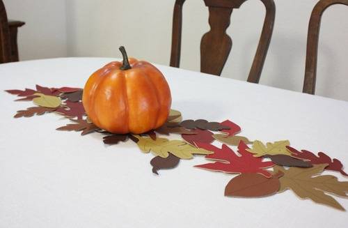 A pumpkin and runner of leaves on a white tablecloth.