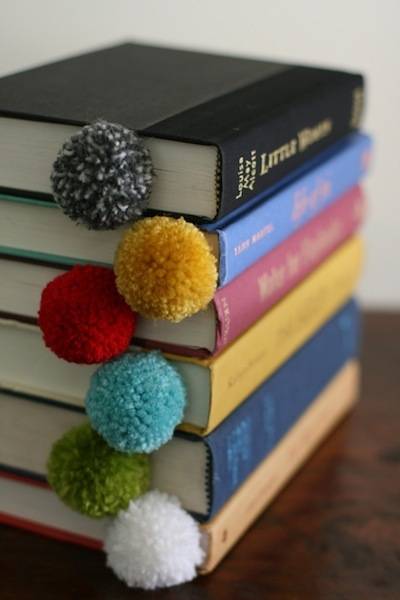Pom poms are visible on the pages on a stack of books.