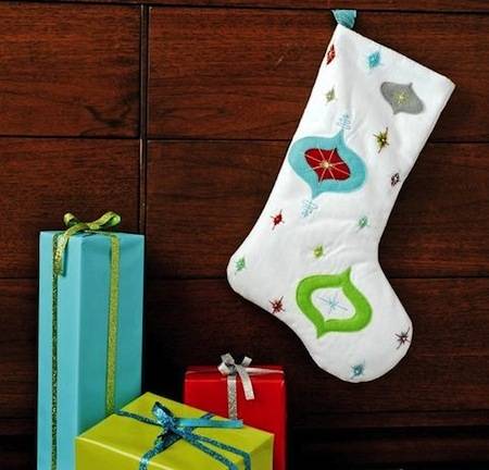 A stocking is hanging on the wall near three colorful gifts.