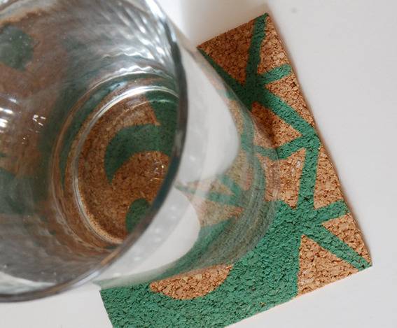 A glass is set on a tan and green colored coaster.