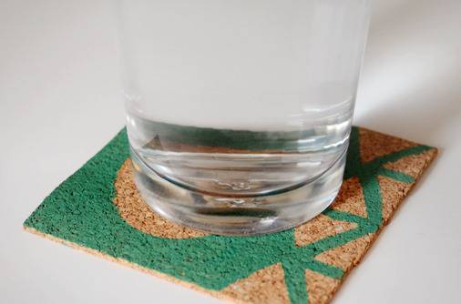 A glass is lying on a green and brown cork coaster.