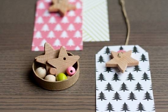 Two star shaped, and other wooden beads in a wooden cup on a table next to two Christmas tree gift tags