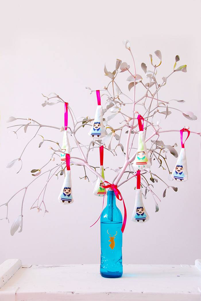 Triangle shape papers with people painted on them are strung with ribbon as ornaments on a tree made of branches