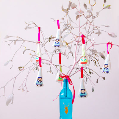 A blue bottle holds water and white branches that have ornaments hanging from them.