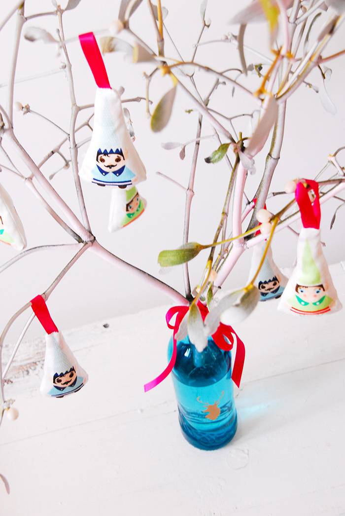 Hanging ornaments decorate branches that are coming out of a bottle.