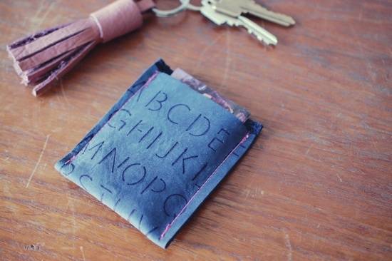 A blue soft wallet with letters stenciled on it next to a pair of keys with a pink leather tassle.