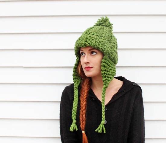 A red-haired woman with a fishtail braid wears a green knit beanie that has earflaps.