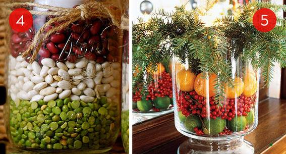 A Christmas themed tabletop decoration is a large jar filled with layers of limes, cranberries, oranges, and pine branches.