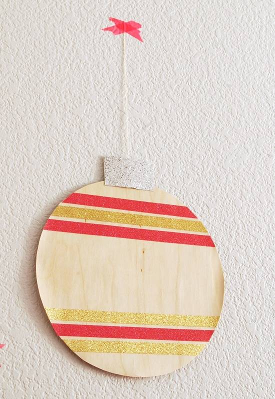 Flat, round hanging Christmas ornament featuring gold and red stripes on pale wood.