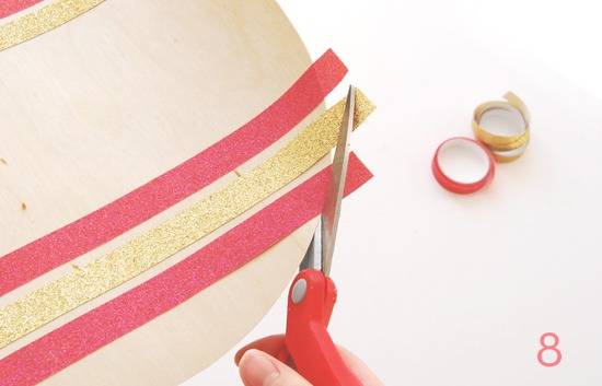 A person using scissors to cut away long edges of ribbon that have been glued to a circle.