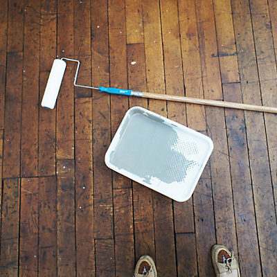 Dark stained wood floor, and a paint tray filled with grey paint.