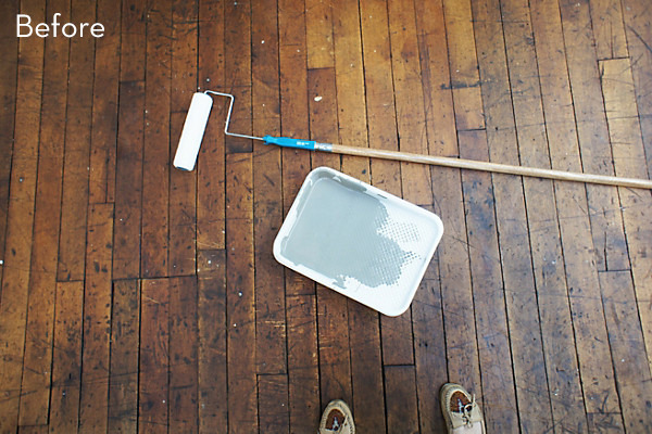 Dark stained wood floor, and a paint tray filled with grey paint.