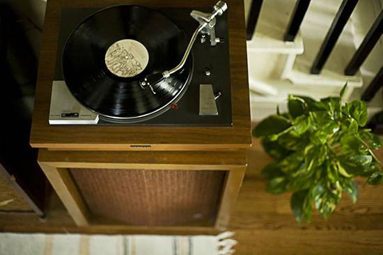 Gramophone player on wooden side table beside the staircase with indoor plant.