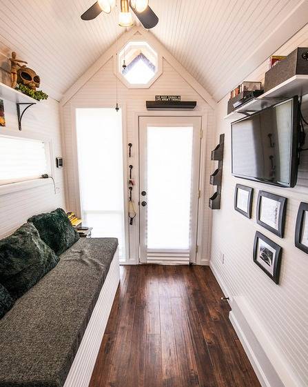 Tiny home with long couch aside, T.V. and photo frames on wall.