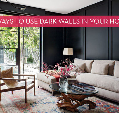 A living room having black walls and beige color sofa set with wooden table and a vase on top of it.