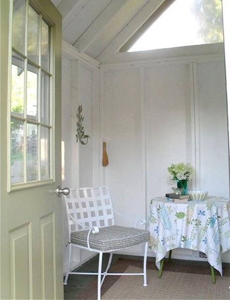 Tiny home with chair, side table covered with cloth and flower vase at top.