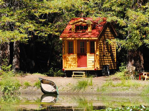 A small wooden house with a red roof and doors, surrounded by trees.