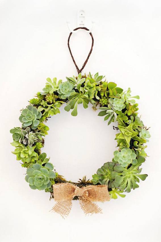 A wreath with a tan bow is hanging from a white wall.