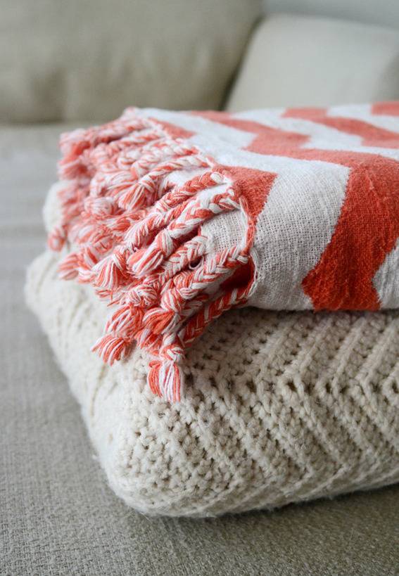 An orange and white blanket on top of a knitted white blanket.