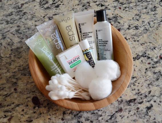 Q-tips, cotton balls, lip gloss, floss and other toiletries in a wooden bowl
