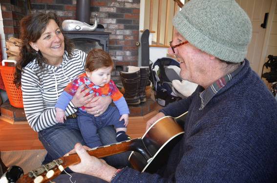 A person is playing guitar and a woman with baby is enjoying it happily.