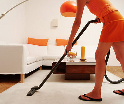 A person in orange is using a vacuum on a gray carpet.
